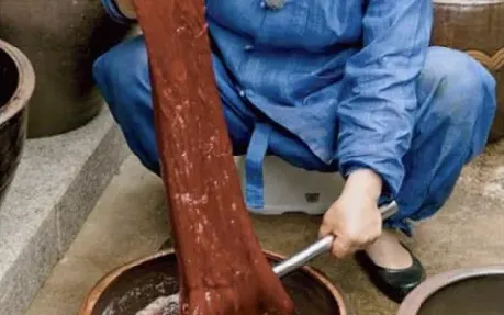 A dyer lifting red-dyed cloth out of a dye bath